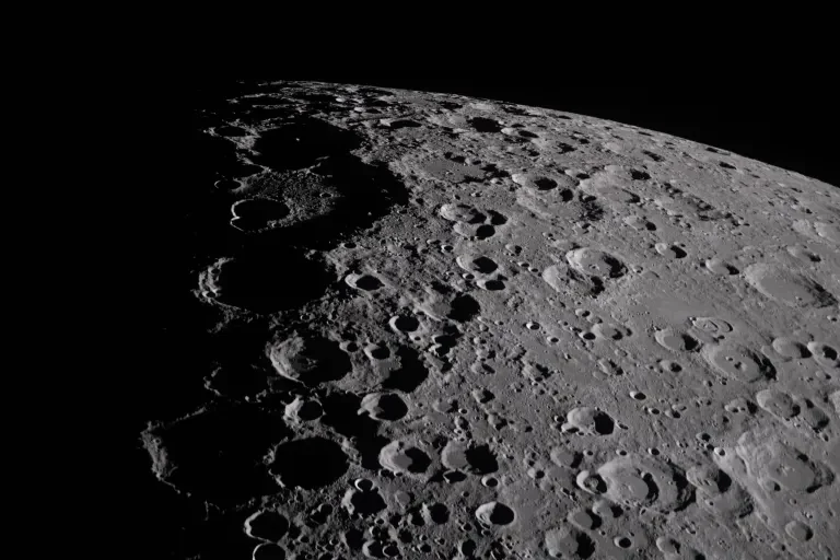 Surface lunaire criblée de cratères, éclairée à droite et plongée dans l’ombre à gauche.