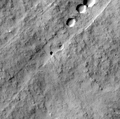 Vue orbitale du flanc du volcan martien Pavonis Mons montrant un puits sombre circulaire qui pourrait être une ouverture vers un tunnel de lave, entouré de terrains et de petits cratères.