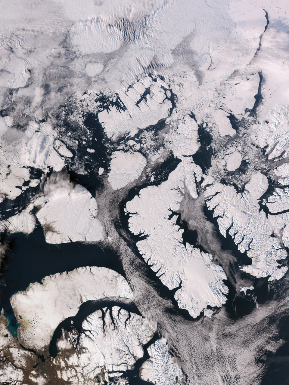 Îles enneigées de l’archipel arctique canadien, fjords profonds et fragments de banquise sur une mer sombre.