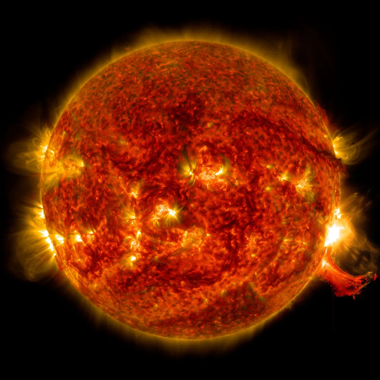 Disque solaire en lumière ultraviolette extrême montrant des régions actives très lumineuses, une protubérance éruptive au limbe droit et la couronne solaire environnante (image composite SOHO).